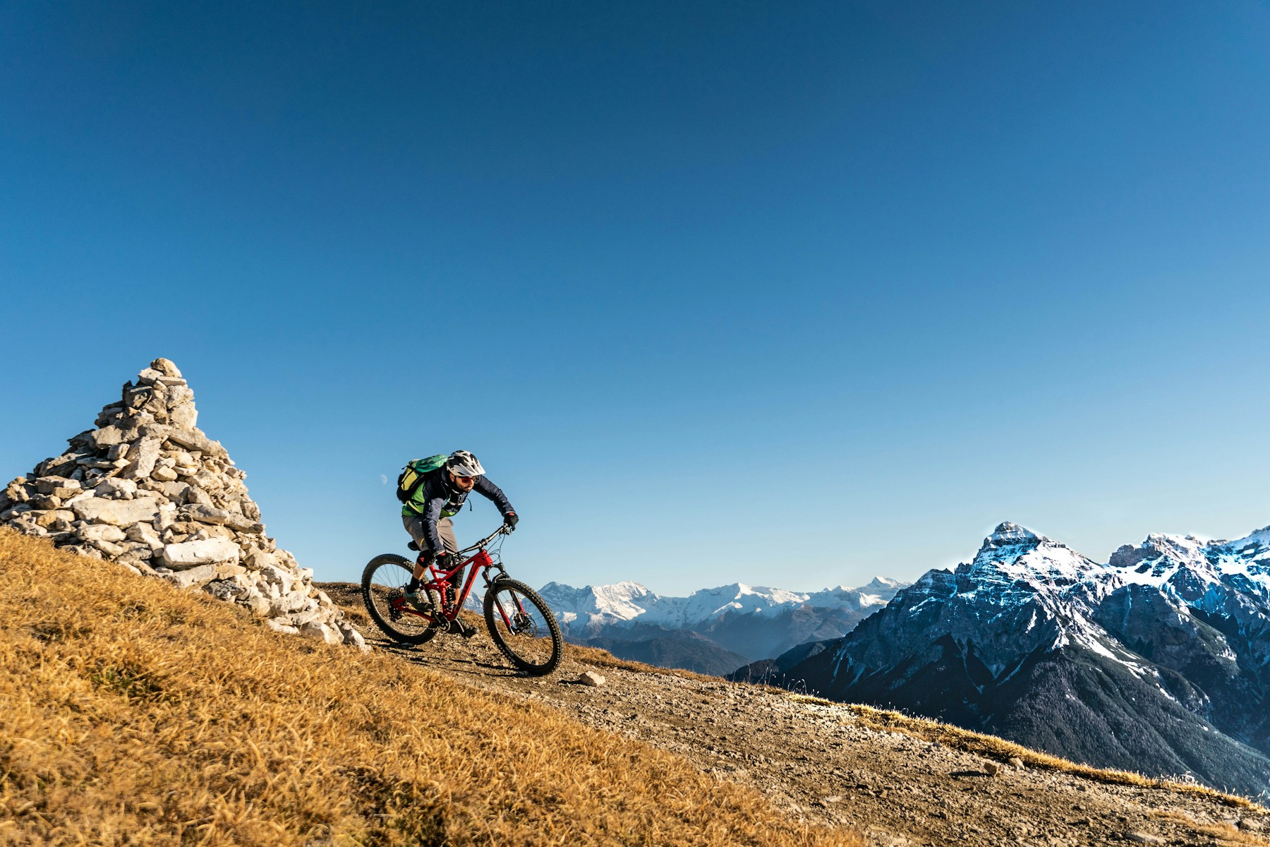 Vététiste descendant un sentier naturel dans un vaste paysage alpin